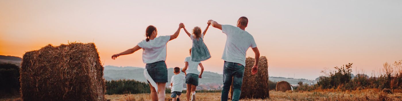 Family running through a hay field at sunset